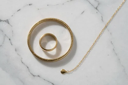 Bijoux plaqués or posés sur marbre blanc — bracelet, bague et collier pour illustrer le prix du plaqué or en 2026