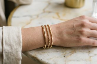 Bracelets fins dorés empilés sur un poignet de femme posé sur du marbre blanc, vue rapprochée